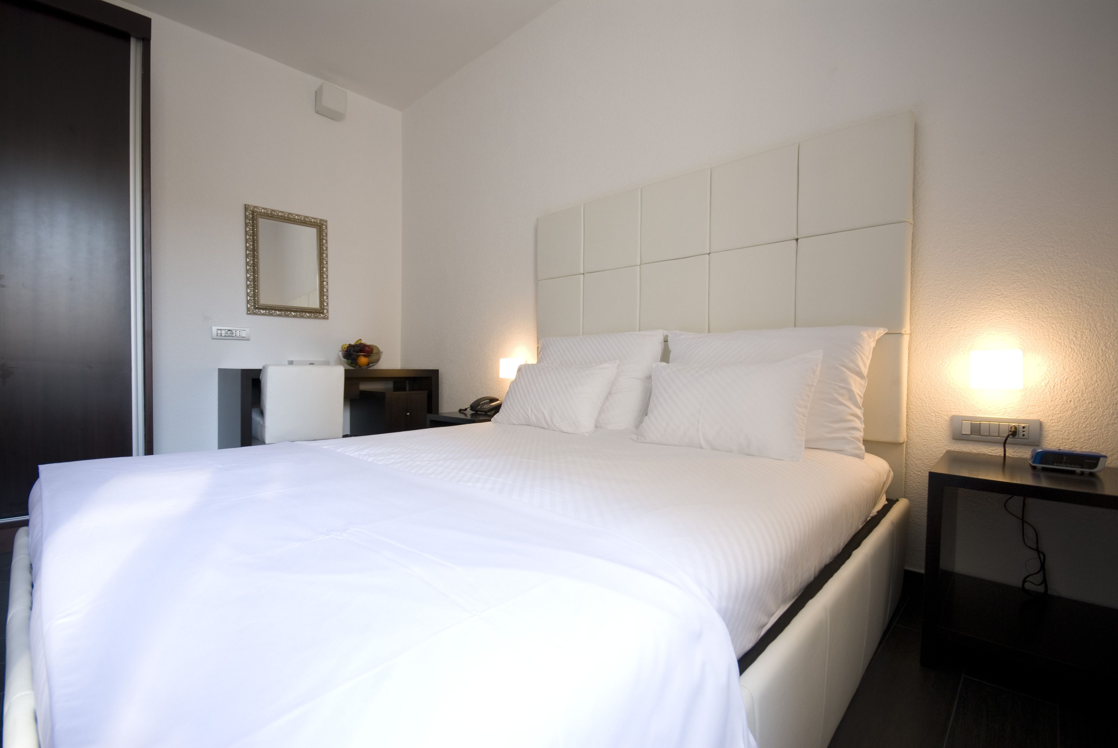 A hotel room with a large bed, a bedside table, a nightstand, a mirror, and a wall socket.