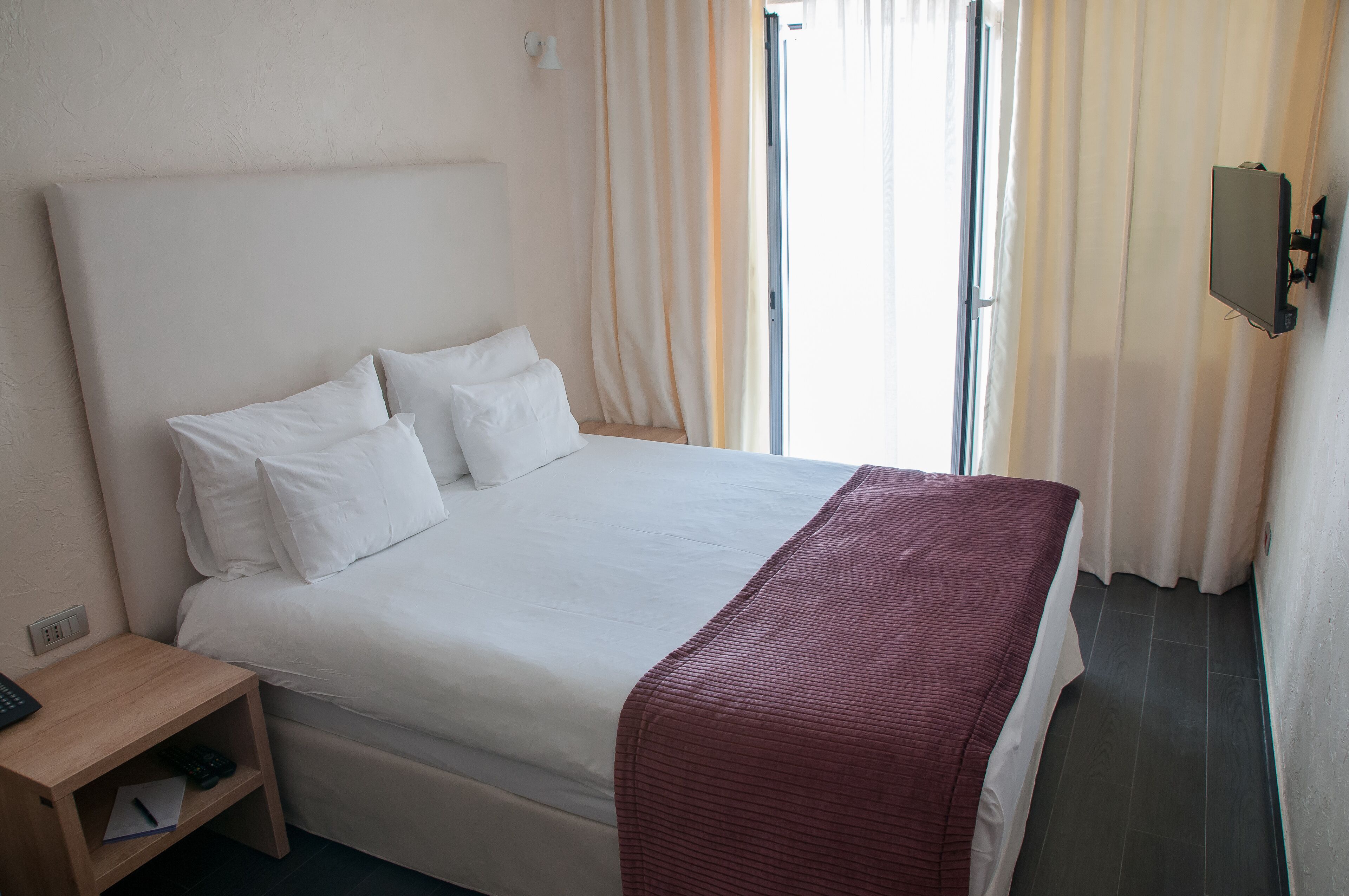 Una habitación de hotel con una cama grande, una mesita de noche de madera y un televisor montado en la pared.