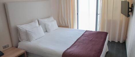 Una habitación de hotel con una cama grande, una mesita de noche de madera y un televisor montado en la pared.