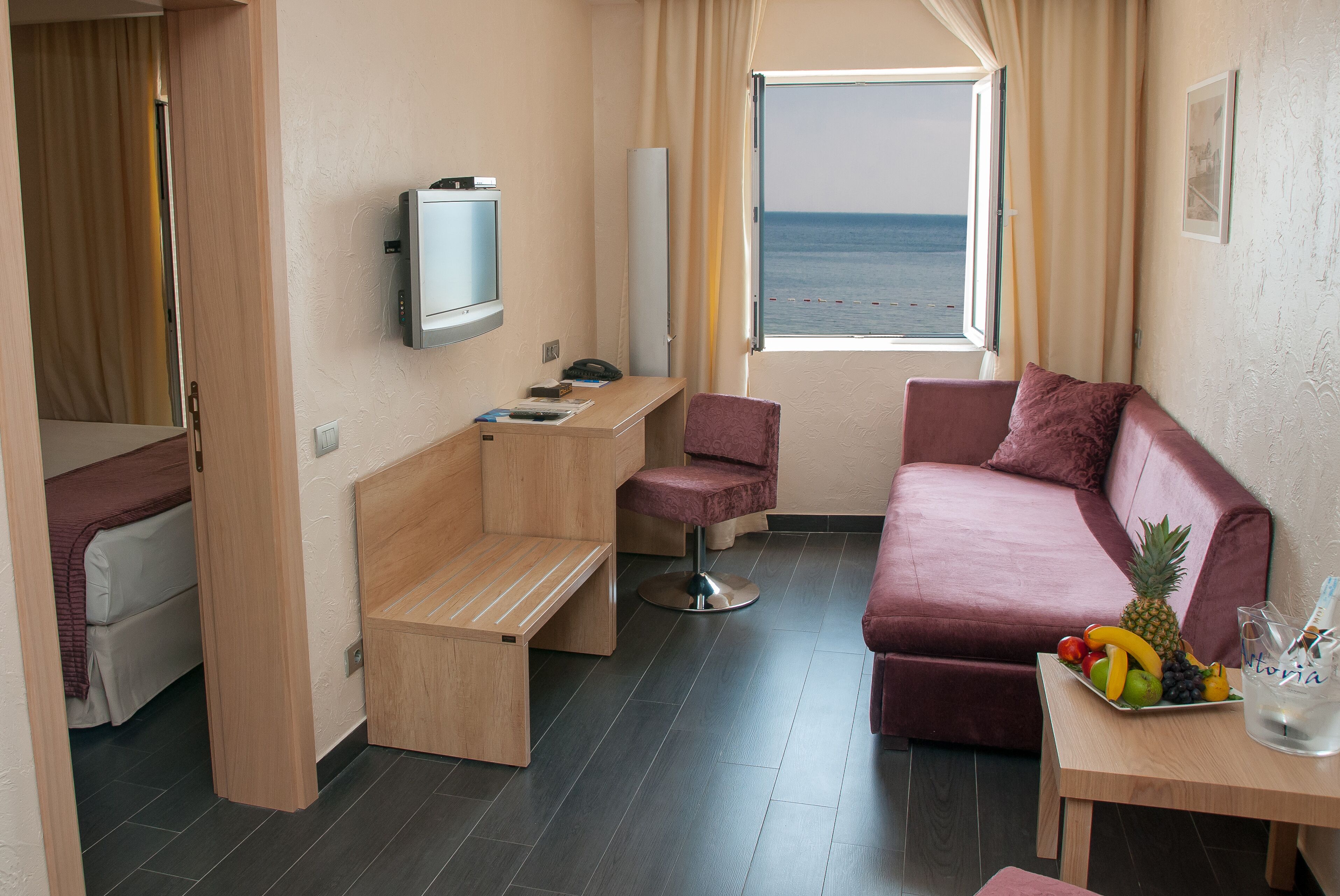 Une chambre d’hôtel compacte comprenant un lit, un petit bureau, une télévision, un canapé et une fenêtre donnant sur la mer.