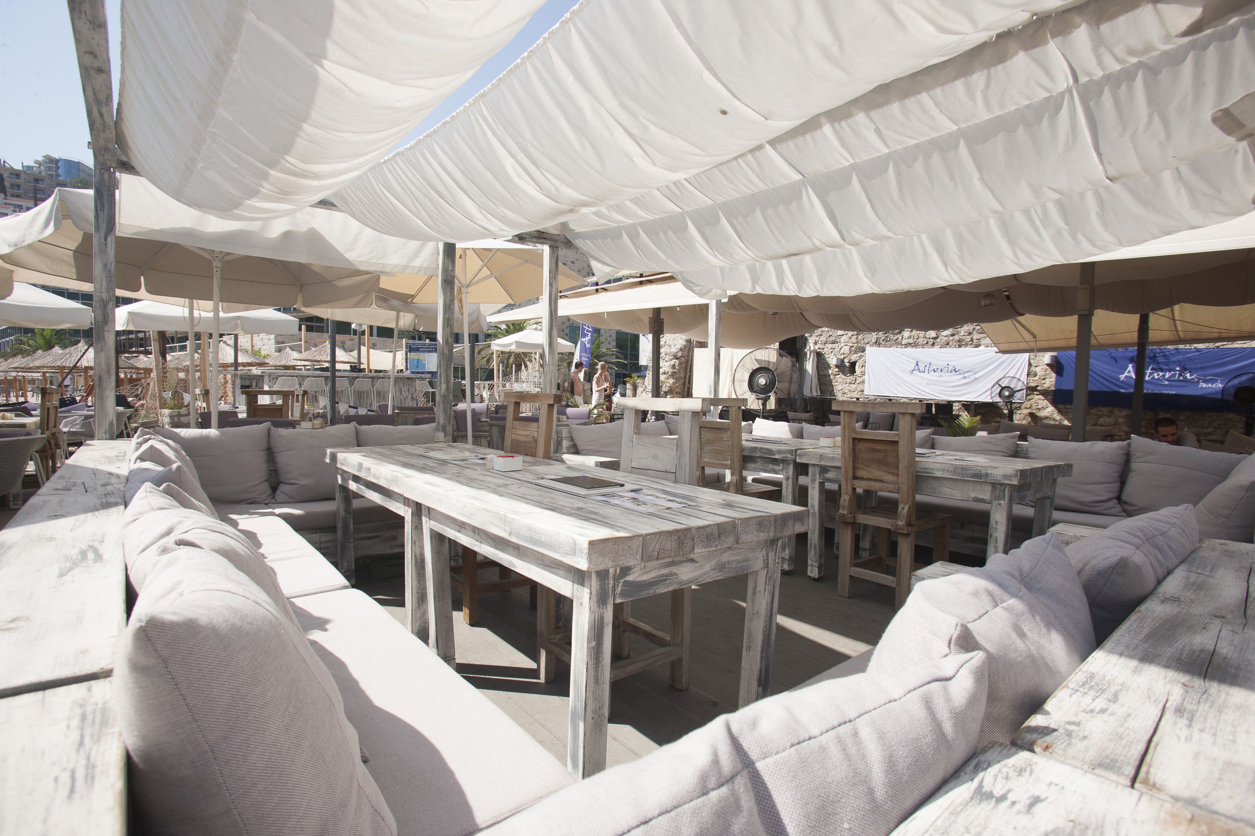 An outdoor seating area with white canopies, wooden tables, and cushioned sofas.