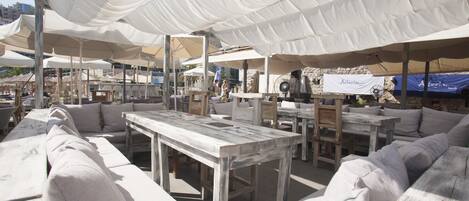 An outdoor seating area with white canopies, wooden tables, and cushioned sofas.