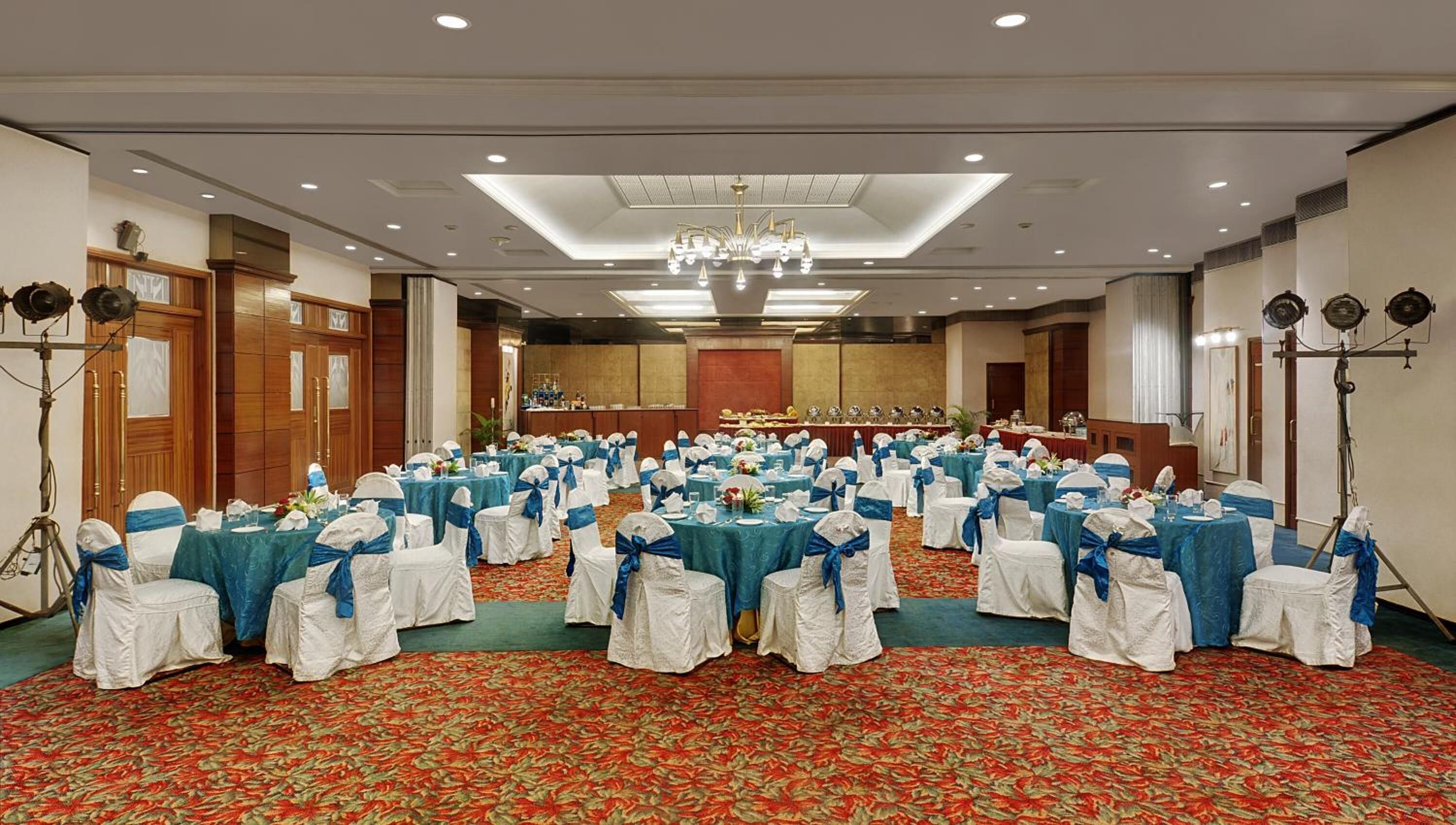 Un salón de banquetes con mesas redondas, sillas blancas y azules, y una alfombra roja.