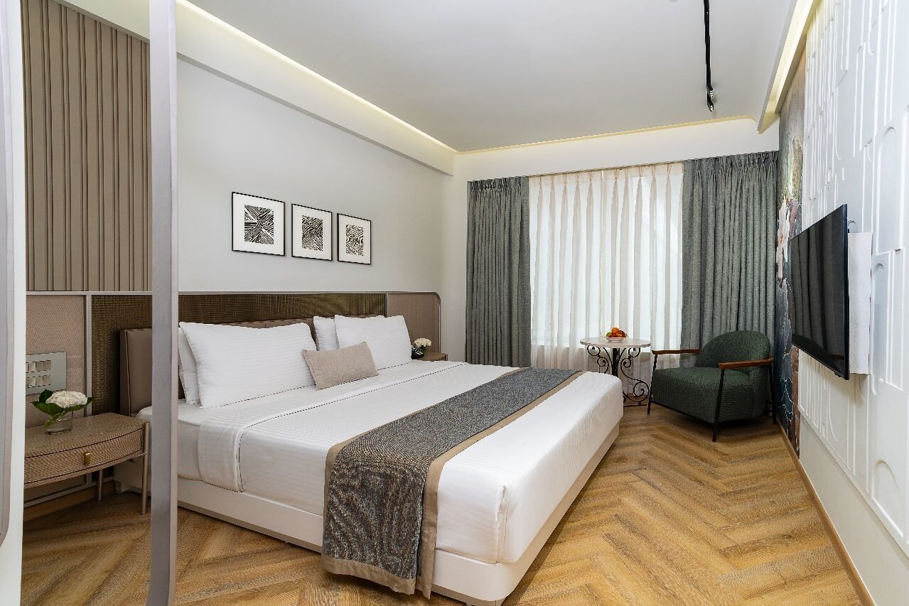 A hotel room with a large bed, a desk, a chair, a TV, and curtains.
