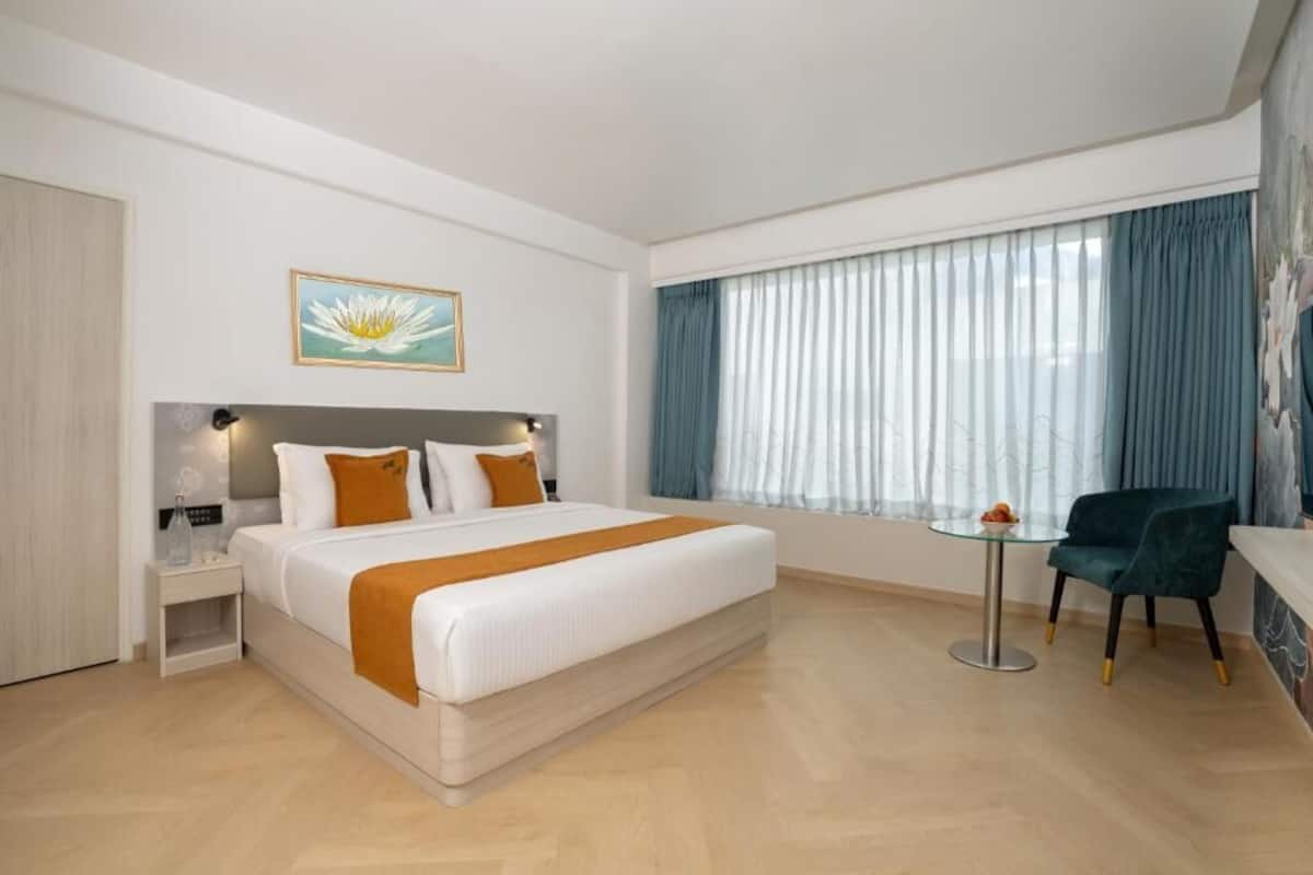 Una habitación de hotel con cama, mesita de noche, una mesa de cristal, una silla y una ventana con cortinas.