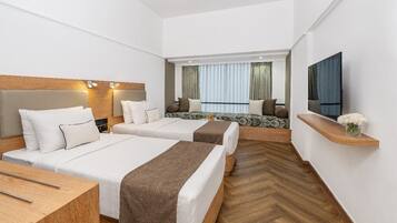 Habitación de hotel con dos camas, cabecera de madera, televisor y una pequeña estantería con flores.