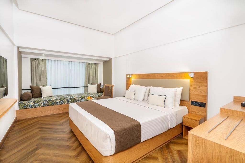 Una habitación de hotel con una cama grande, una mesita de noche, un escritorio y una ventana con cortinas.