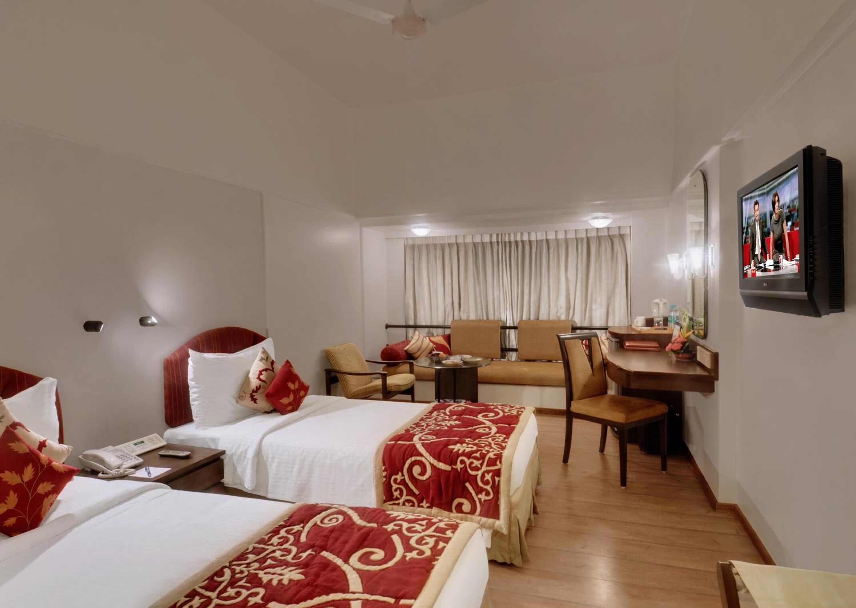 A hotel room with two beds, a sofa, a desk, and a television.