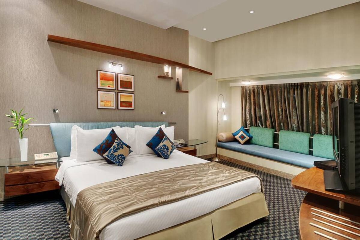 Una habitación de hotel con una cama grande, una zona de estar con sofá, televisión y una planta.