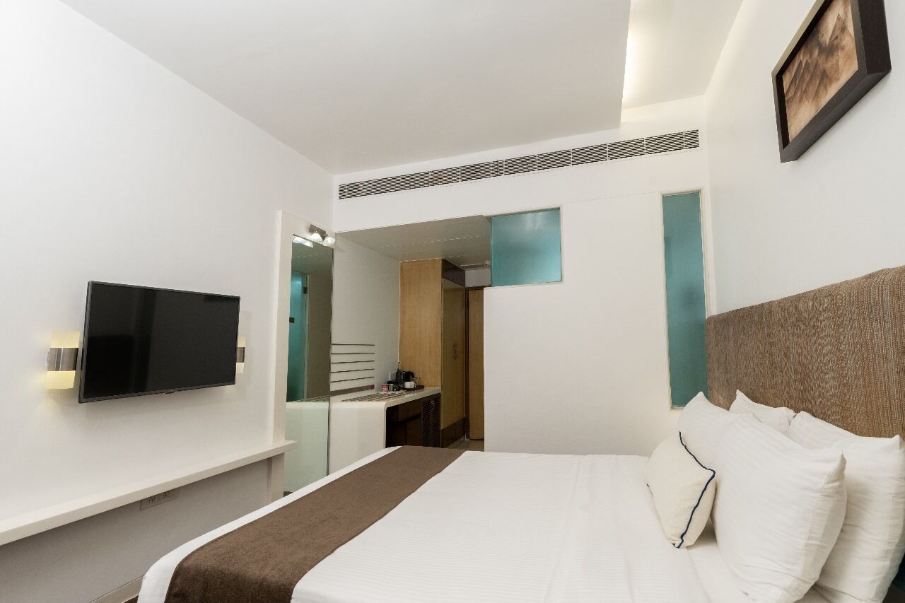 Ein Hotelzimmer mit einem Bett, einem Flachbildfernseher, einem Schreibtisch und einem Spiegel.