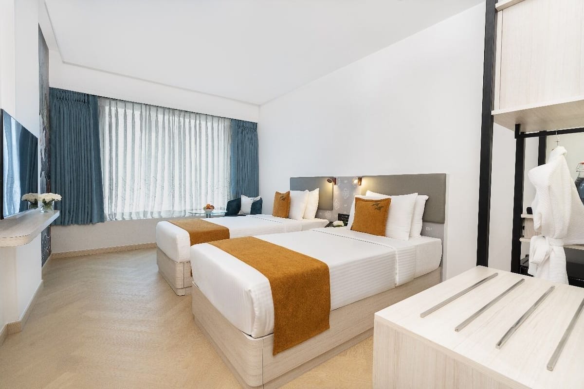 Una habitación de hotel con dos camas, una zona de estar, un tocador con espejo y una ventana con cortinas.