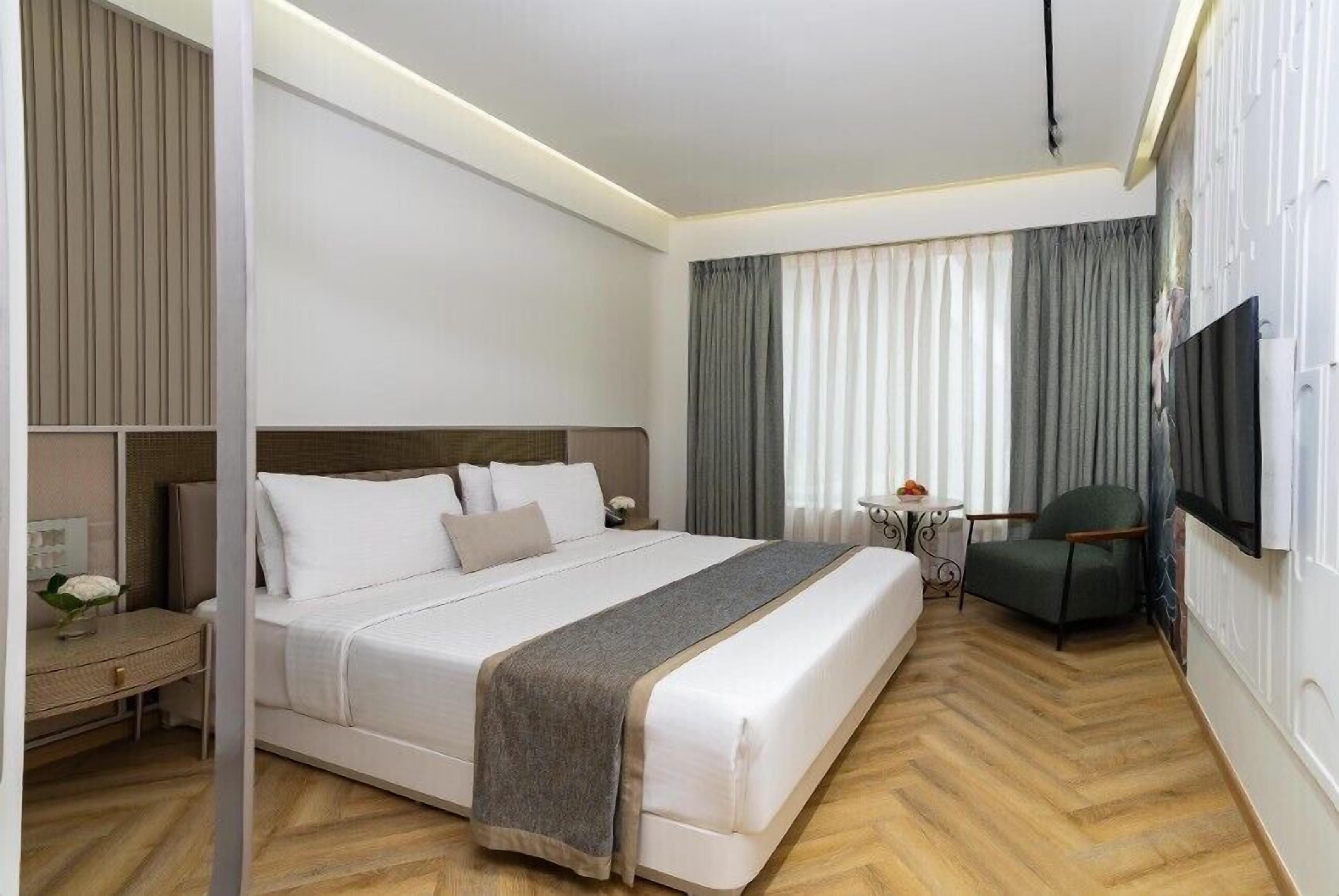 Habitación de hotel con una cama grande, un escritorio, una silla, un televisor y una ventana con cortinas.