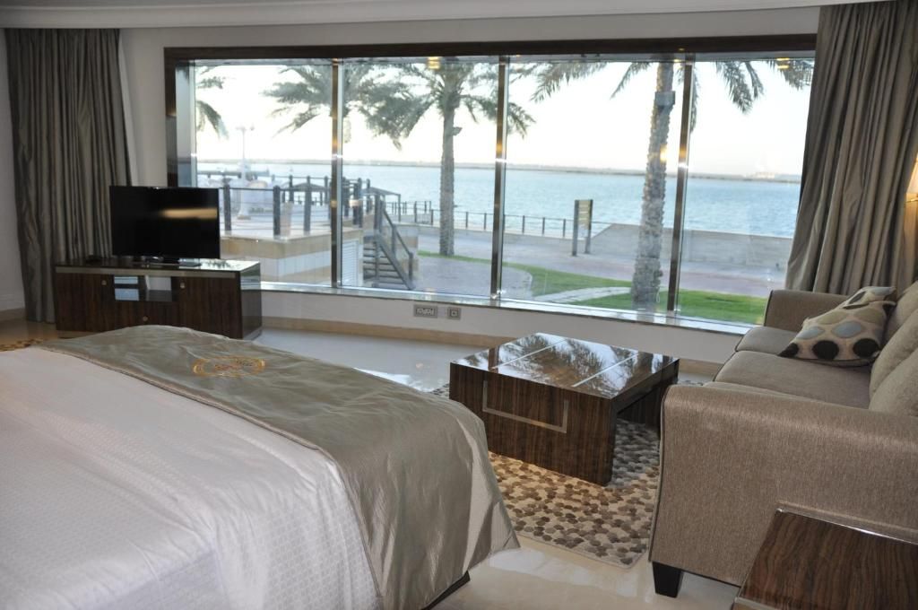 Habitación de hotel con un amplio ventanal que ofrece vistas a una playa y palmeras.