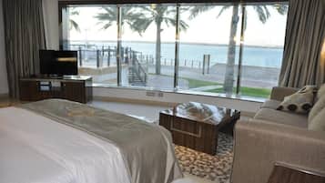 Habitación de hotel con un amplio ventanal que ofrece vistas a una playa y palmeras.