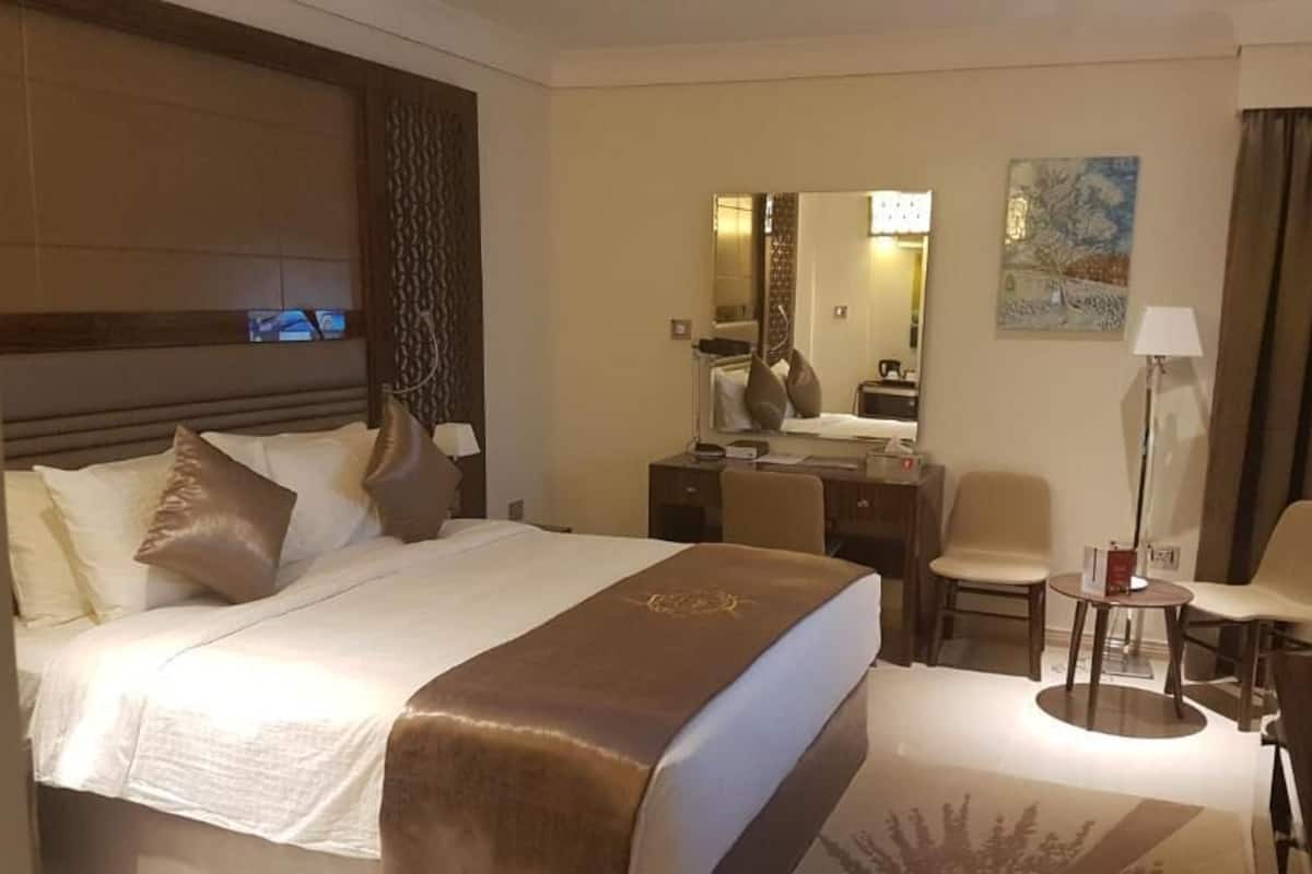 Quarto de hotel com uma cama grande, uma escrivaninha, uma cadeira, uma televisão e um quadro na parede.