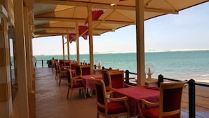 An outdoor dining area with tables and chairs, a view of the sea, and a covered walkway. - Tio Sea Resort Al Khor (Al Khor)