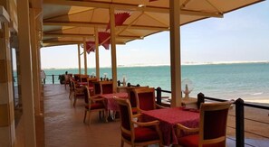 Un restaurante frente al mar con terraza, mesas y sillas de madera.