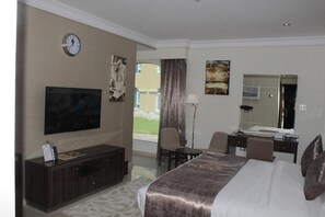 Habitación de hotel con cama, escritorio, silla, televisor, reloj y ventana con cortinas.