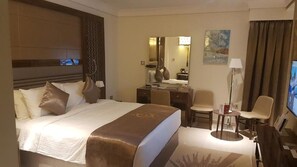 Una habitación de hotel con una cama grande, un escritorio, una silla, un televisor y un cuadro en la pared.