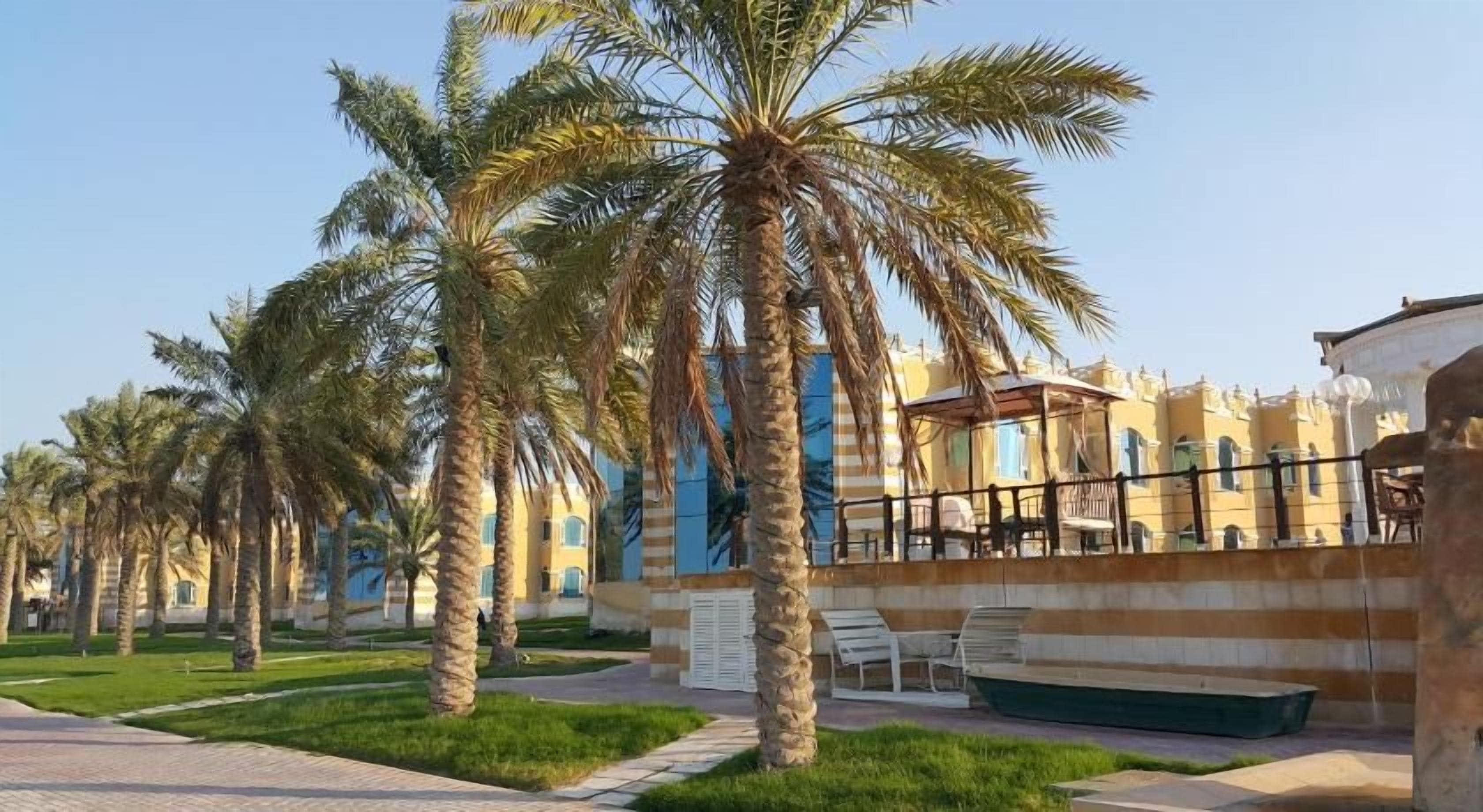 A courtyard with palm trees, a pool, and a building with striped walls.