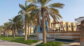 A courtyard with palm trees, a pool, and a building with striped walls. - Tio Sea Resort Al Khor (Al Khor)