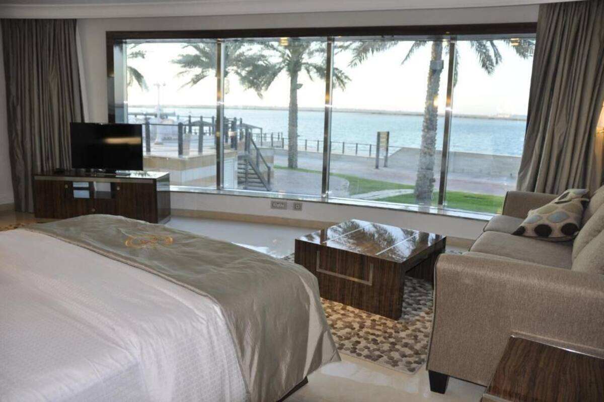 Quarto de hotel com uma janela ampla que oferece vista para uma praia e palmeiras.