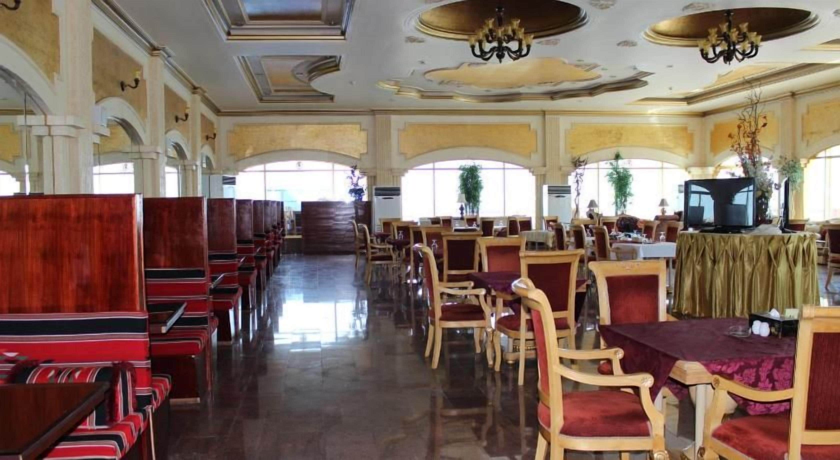 Un comedor amplio con filas de mesas y sillas de madera, un candelabro y ventanas grandes.