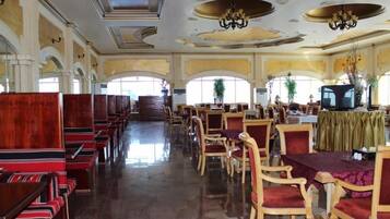 Un comedor amplio con filas de mesas y sillas de madera, un candelabro y ventanas grandes.
