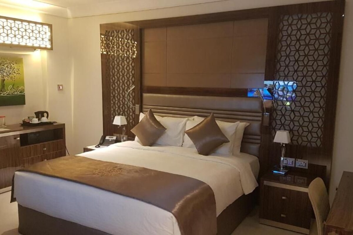 Habitación de hotel con una cama grande, un escritorio y una silla. Hay un cuadro en la pared y un panel decorativo.