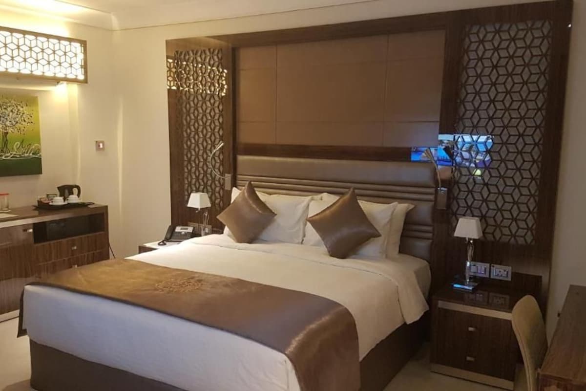 Habitación de hotel con una cama grande, un escritorio y una silla. Hay un cuadro en la pared y un panel decorativo.