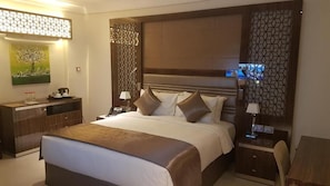 Habitación de hotel con una cama grande, un escritorio y una silla. Hay un cuadro en la pared y un panel decorativo.