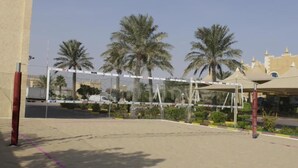 A volleyball court with a net, palm trees, and a building in the background. - Tio Sea Resort Al Khor (Al Khor)