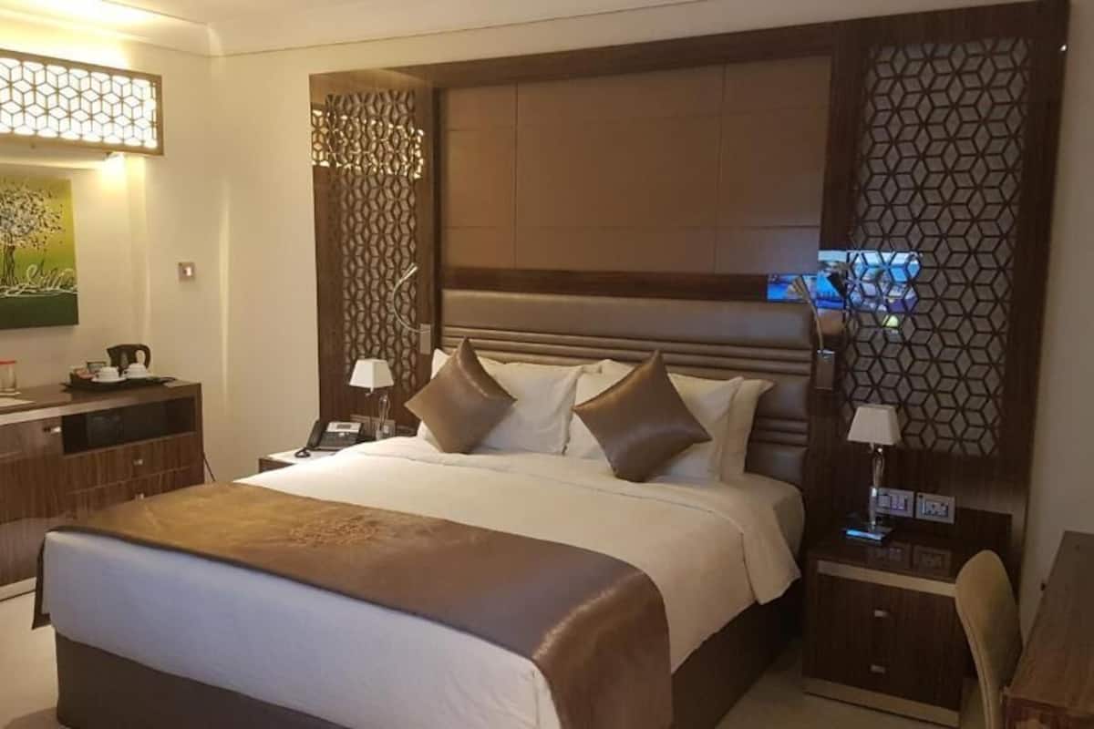 Quarto de hotel com uma cama grande, uma escrivaninha e uma cadeira. Há um quadro na parede e um painel decorativo.