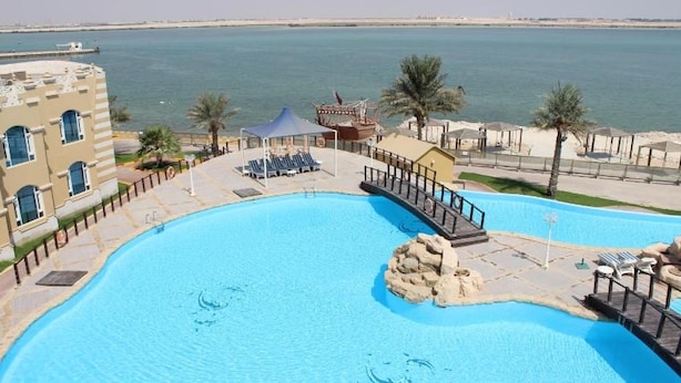 A large swimming pool with a stone feature, surrounded by lounge chairs and a building with a view of the sea. - Tio Sea Resort Al Khor (Al Khor)