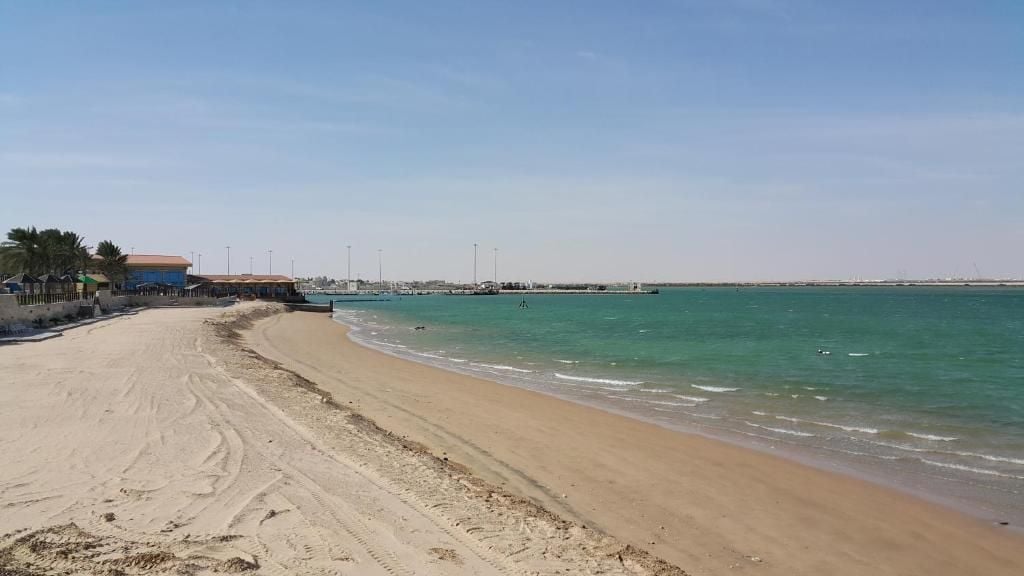 A beach with a sandy shore, a pier in the distance, and a clear sky.