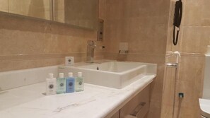 Un baño con un lavamanos grande blanco, un espejo y una ducha. Hay tres botellas de jabón líquido en el lavamanos.