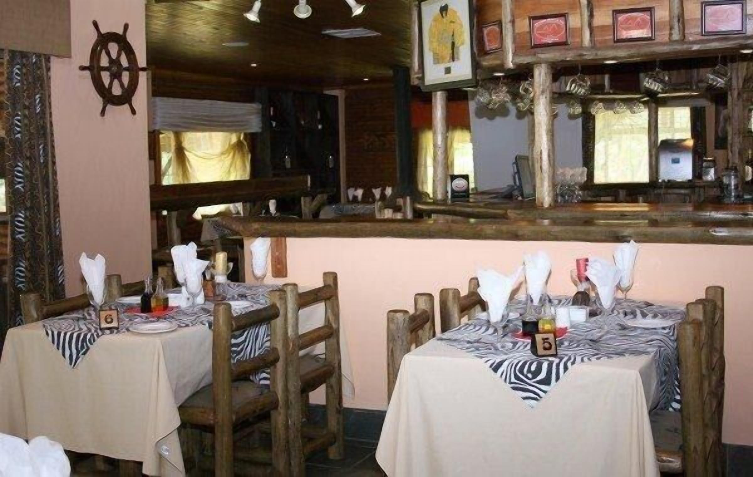A restaurant with wooden tables and chairs, a bar area, and a ship's wheel decoration on the wall.