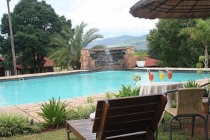 Une piscine agrémentée d’une cascade, entourée de verdure, avec une table et des chaises à proximité.