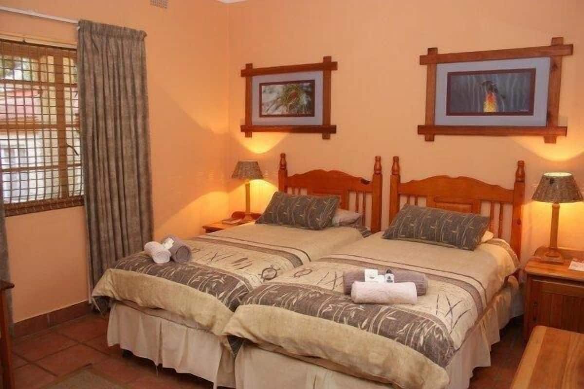 A double room with two beds, each with a wooden headboard, a window with curtains, and two wall-mounted picture frames.