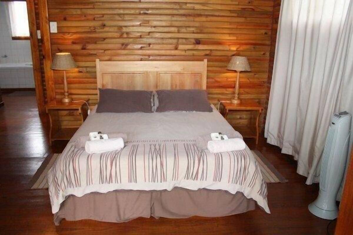 A wooden-paneled bedroom with a bed, two bedside lamps, and a window with curtains.