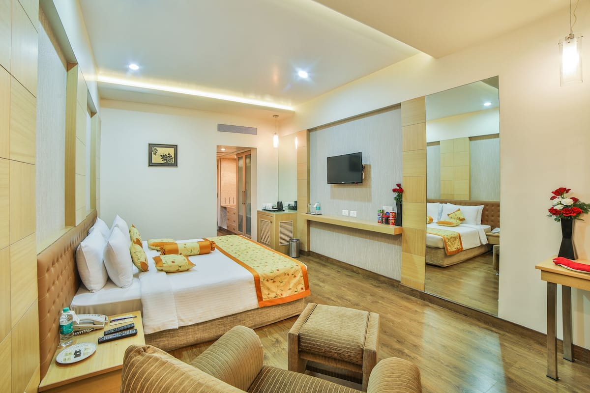 A hotel room with a bed, a desk with a chair, a TV, and a large mirror.
