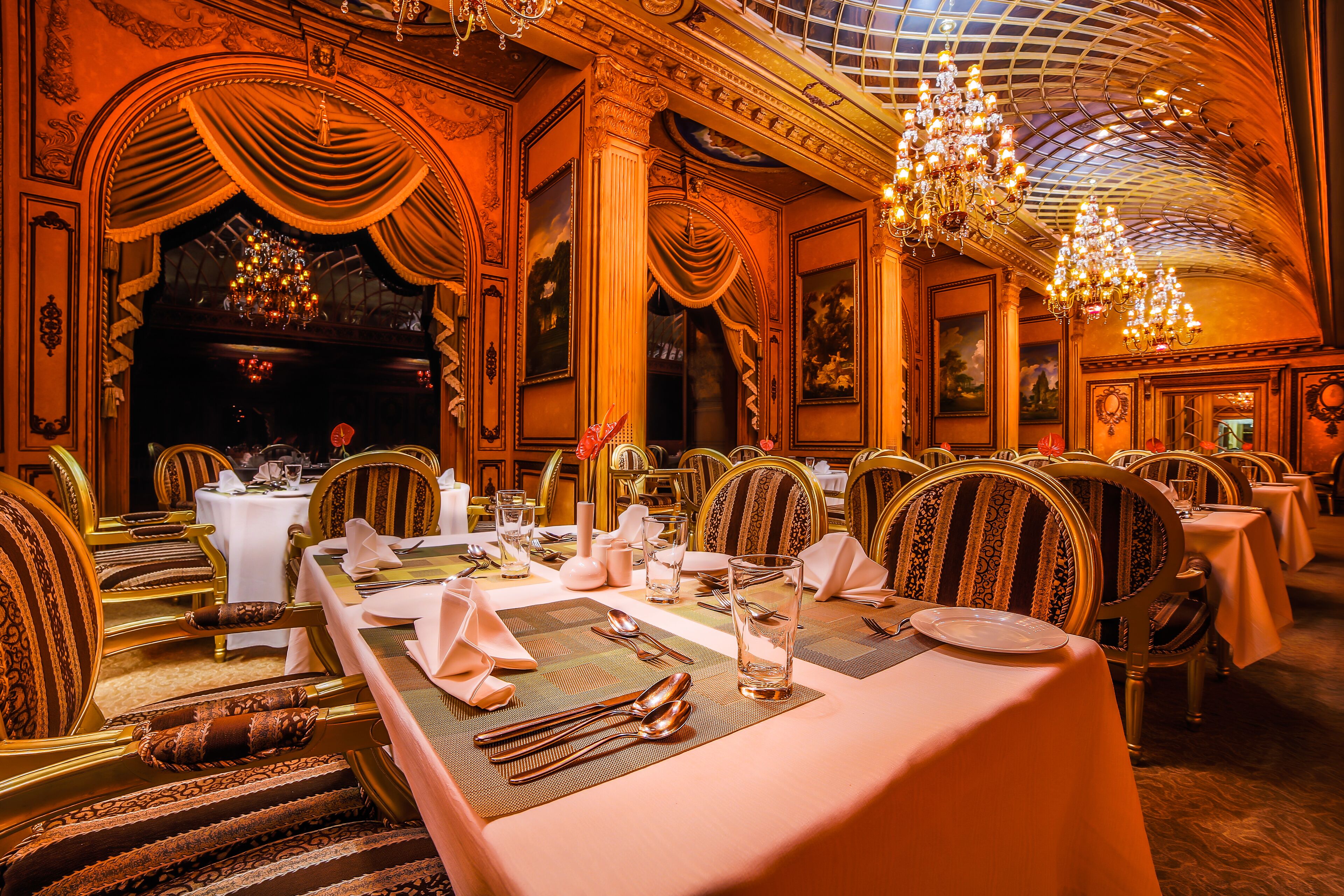 A luxurious dining room with ornate chandeliers, elegant table settings, and classic architecture.
