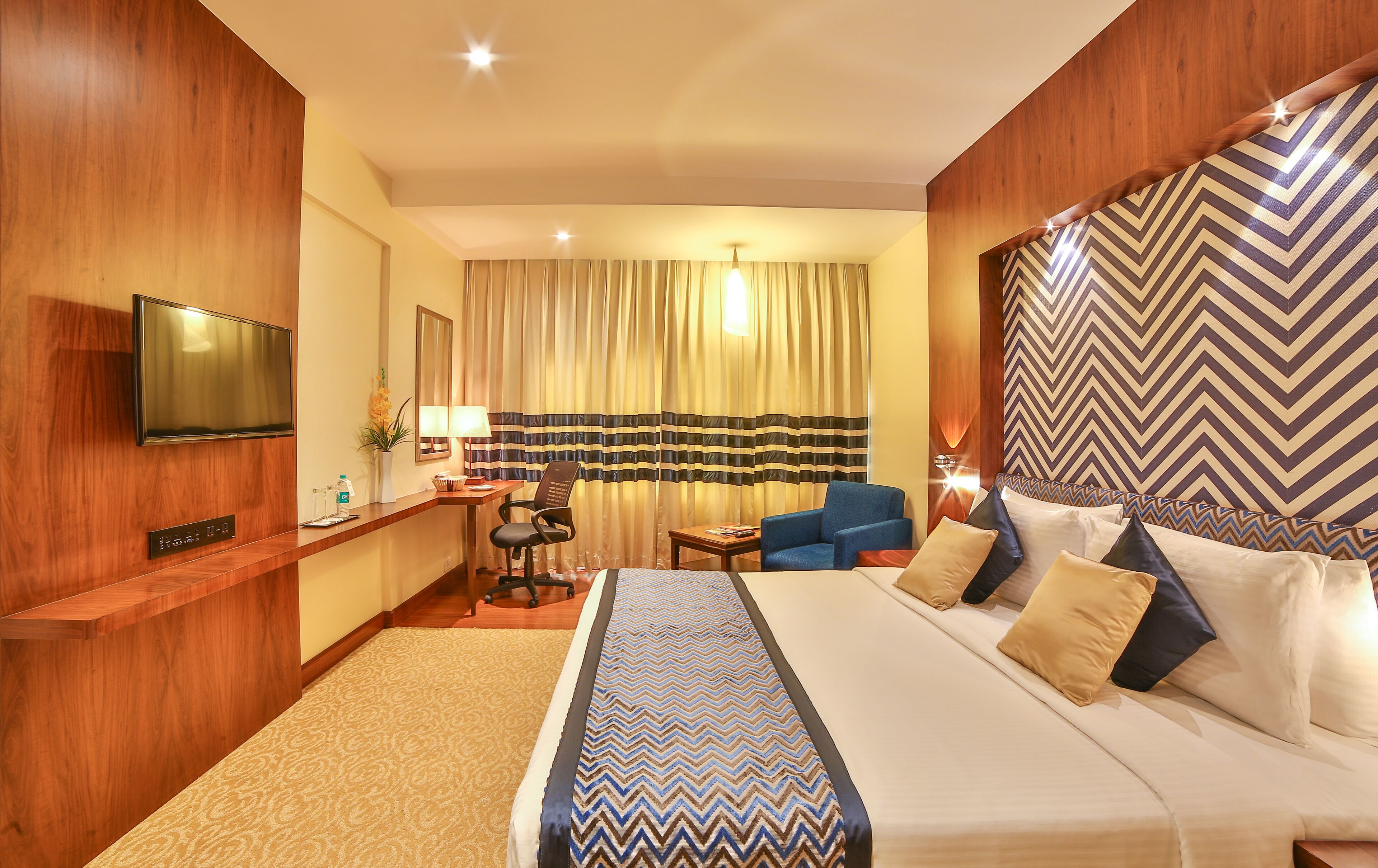 Une chambre d’hôtel avec un grand lit, un bureau avec une chaise, une télévision et un mur décoré de motifs.