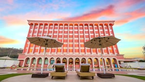 Un hotel con una amplia fachada roja, varios balcones y mobiliario exterior con sombrillas.