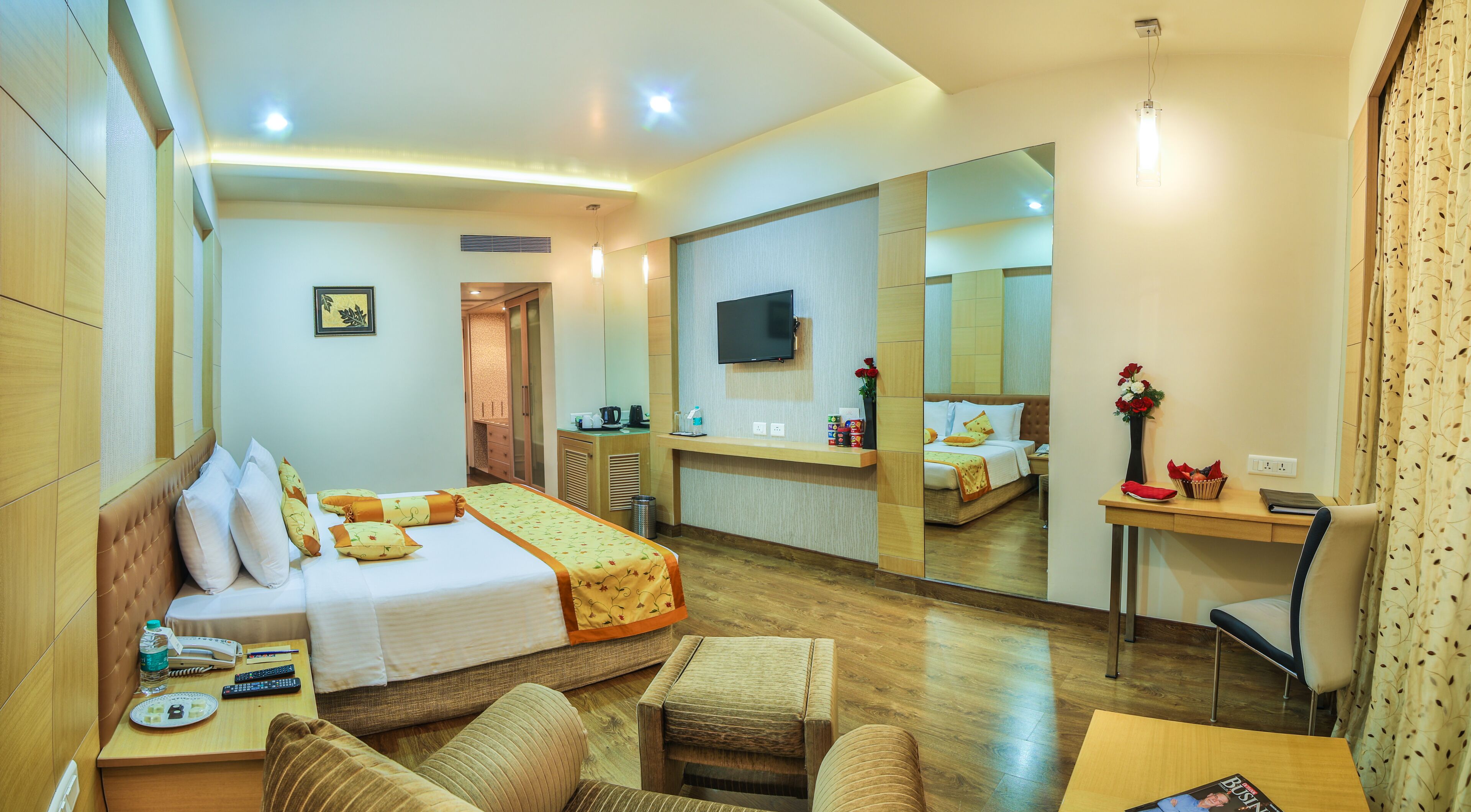 A hotel room with a bed, a desk, a chair, a sofa, a mirror, and a TV.