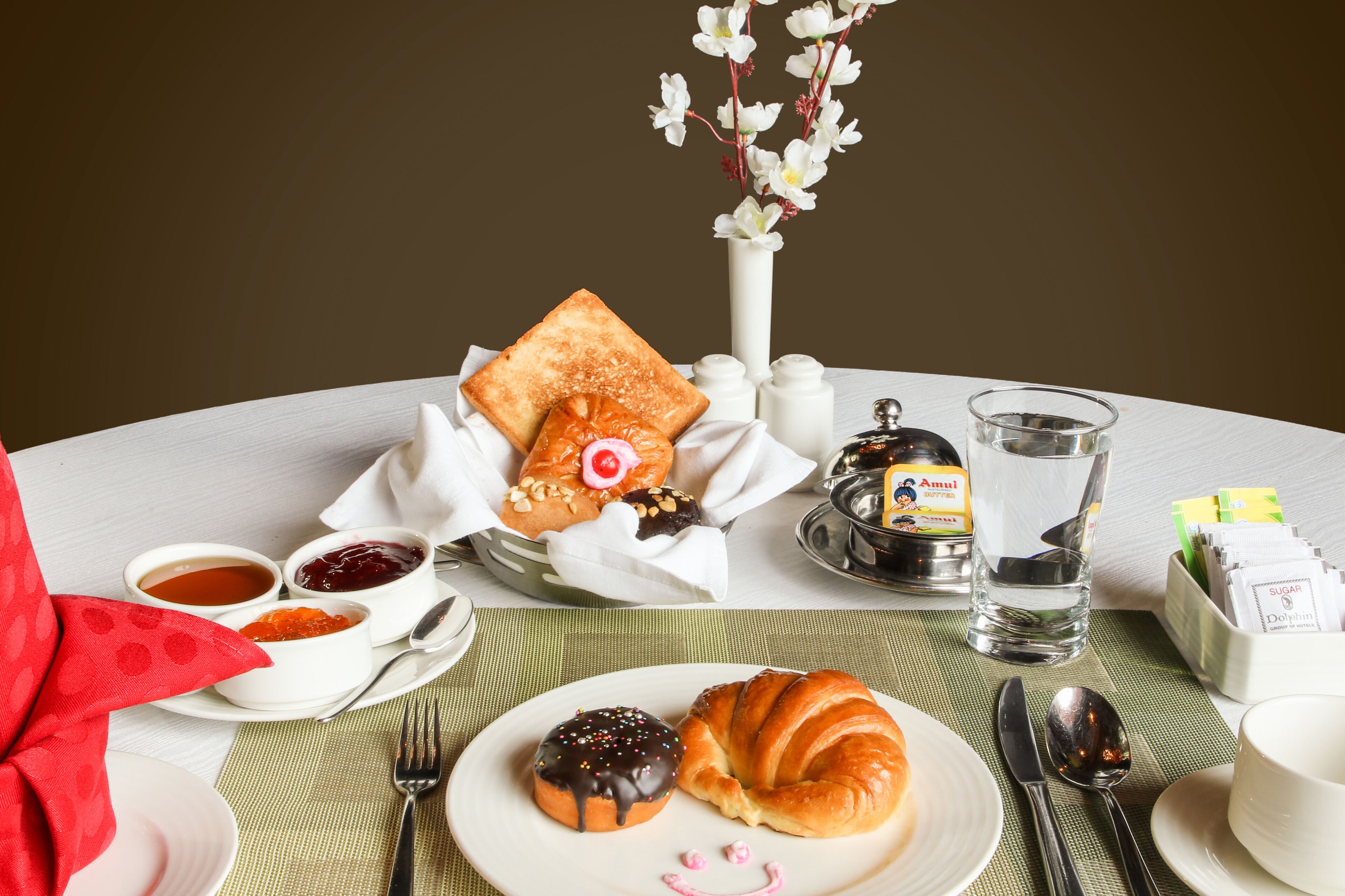 Une table dressée pour le petit-déjeuner avec des toasts, des croissants, de la confiture et un pot de beurre Amul.