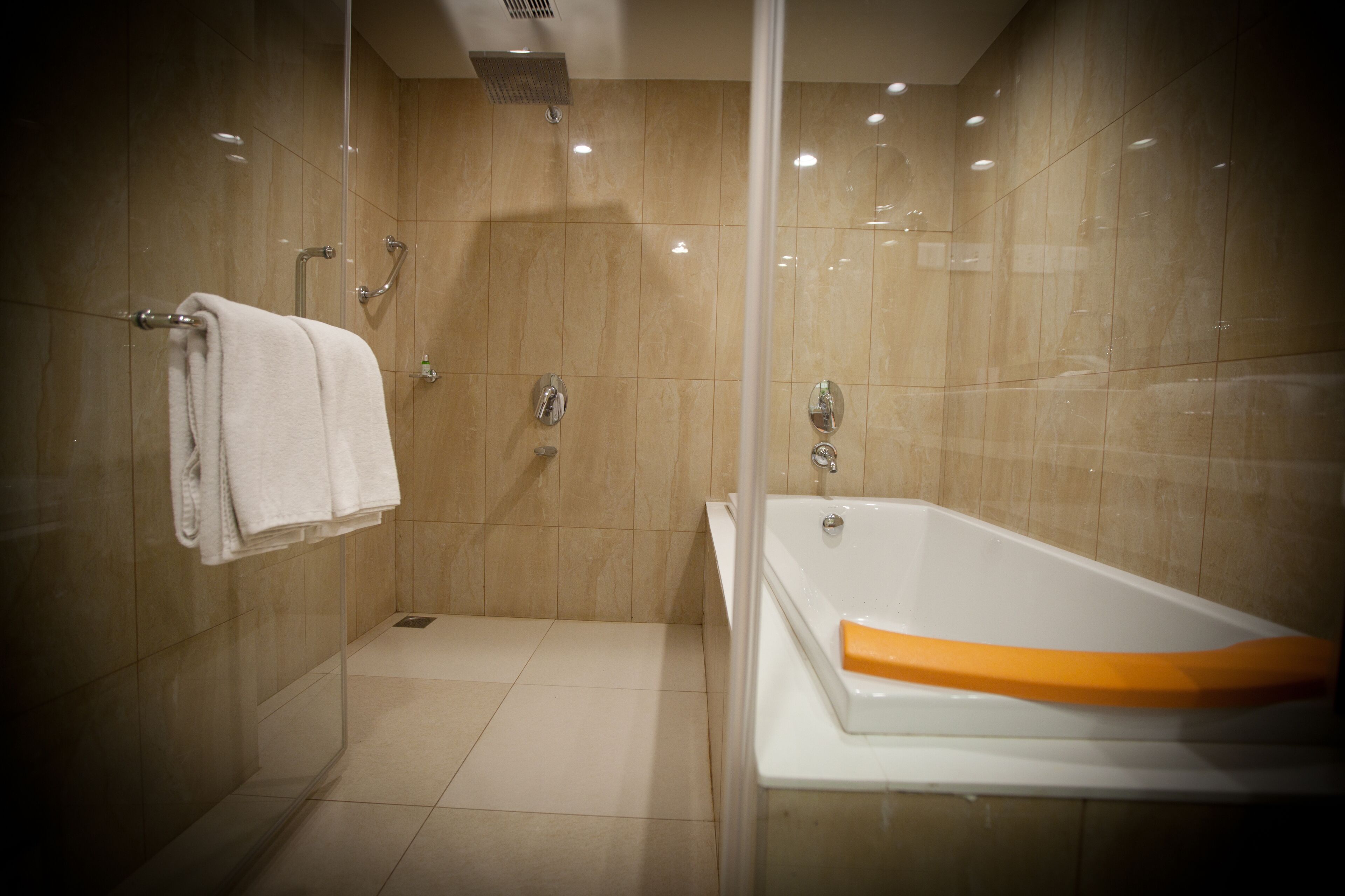 Une salle de bain moderne avec une douche à parois de verre, une baignoire blanche agrémentée d’une touche de couleur orange, et un porte-serviettes avec des serviettes pliées.