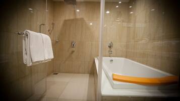 Une salle de bain moderne avec une douche à parois de verre, une baignoire blanche agrémentée d’une touche de couleur orange, et un porte-serviettes avec des serviettes pliées.