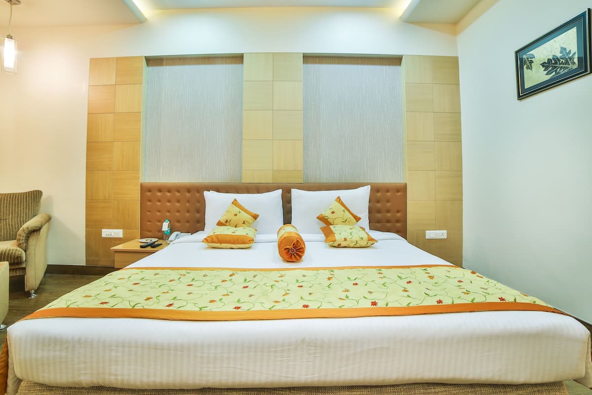 A hotel room with a large bed, a nightstand, a chair, and a framed picture on the wall.