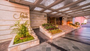Fachada de hotel de mármol, con una escalera que conduce a la entrada y plantas en macetas a lo largo de los escalones.